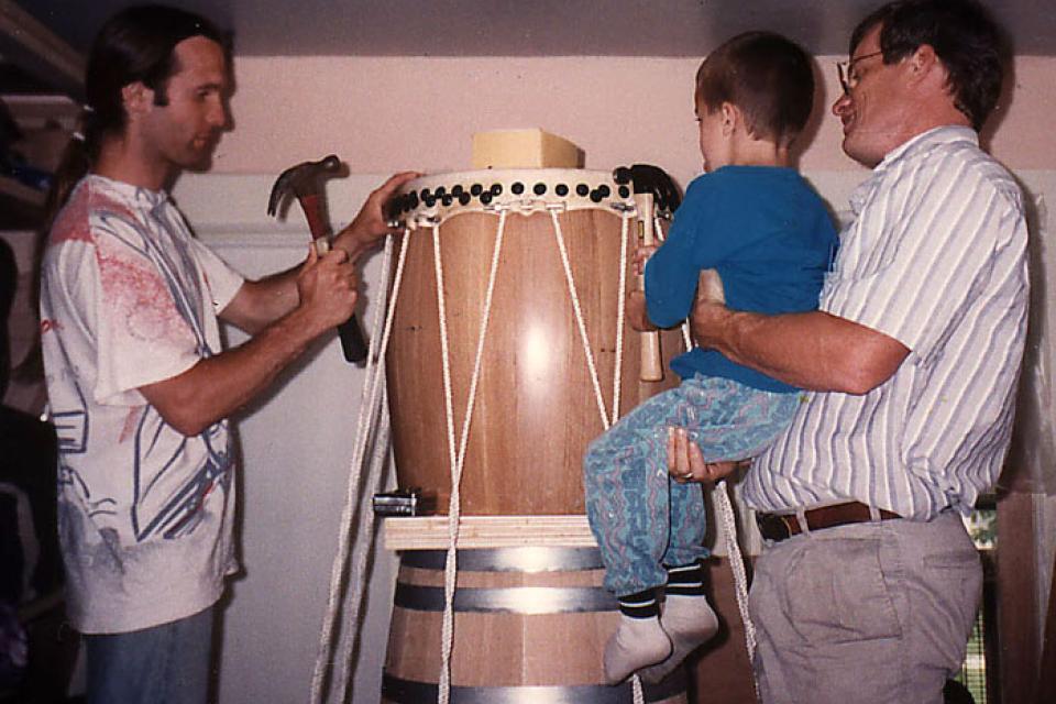 Two men tack the head of their new taiko while a small child looks on